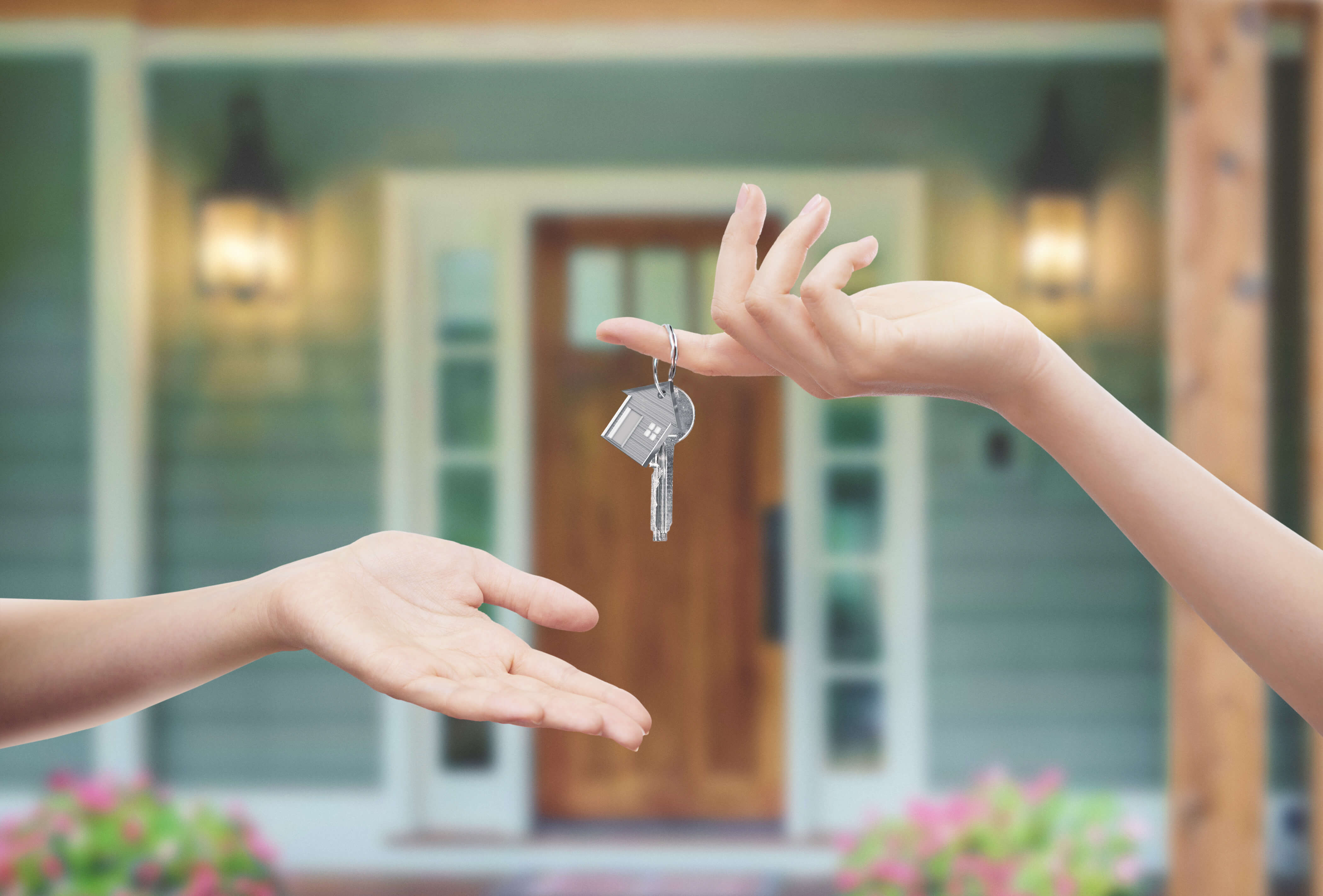 Hand passing house keys to another in front of a home, symbolizing helpful homebuying resources and guidance for new homeowners.
