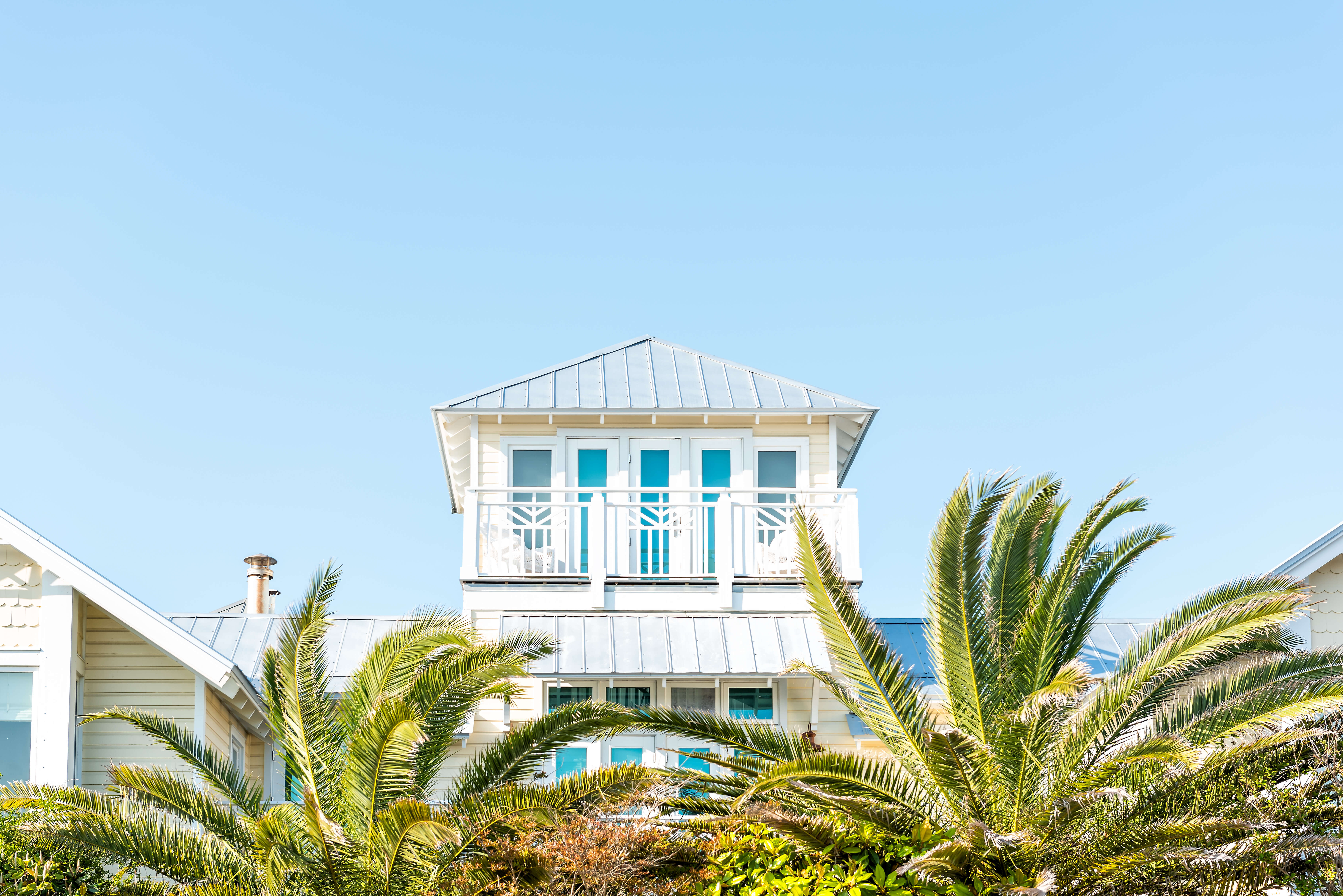 Coastal vacation home with bright balcony and palm trees, representing the importance of short-term rental insurance to protect property and income when renting to guests