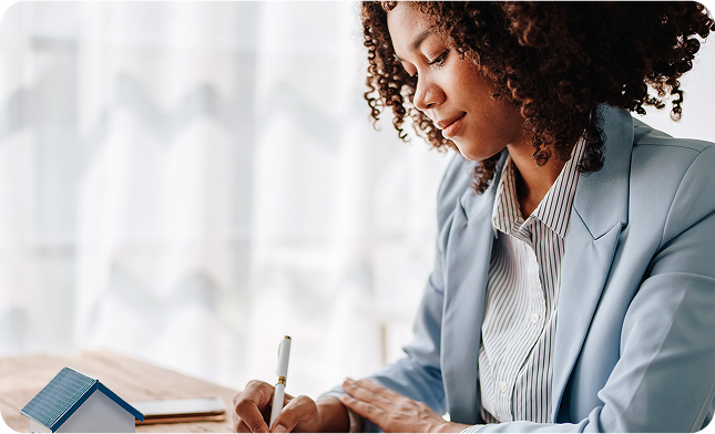 Professional woman reviewing paperwork at a desk with a small model house nearby, representing homeowners in Georgia exploring insurance discounts and savings opportunities